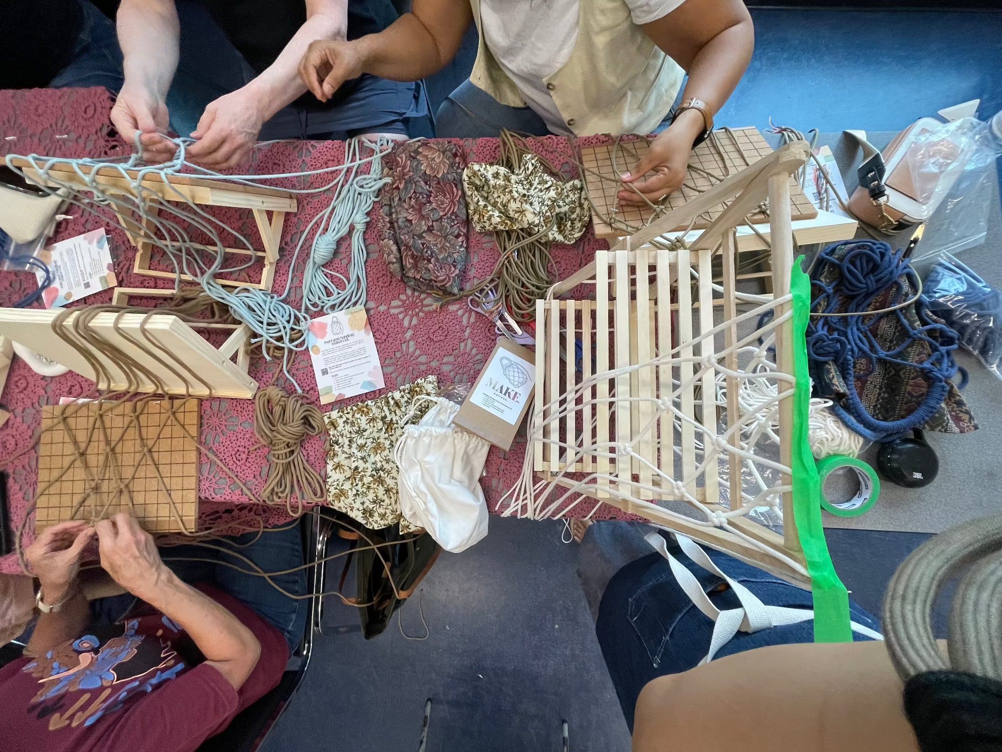 People working on weaving projects at a table with materials and tools.